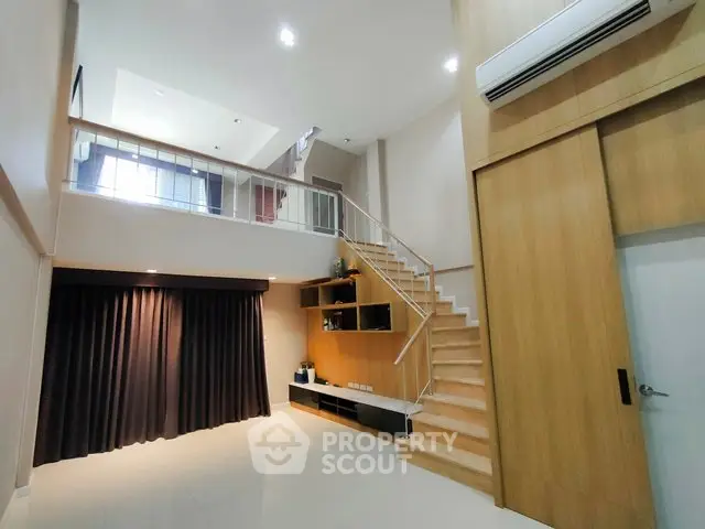 Modern duplex living room with high ceiling and staircase, featuring sleek wooden accents and ample natural light.