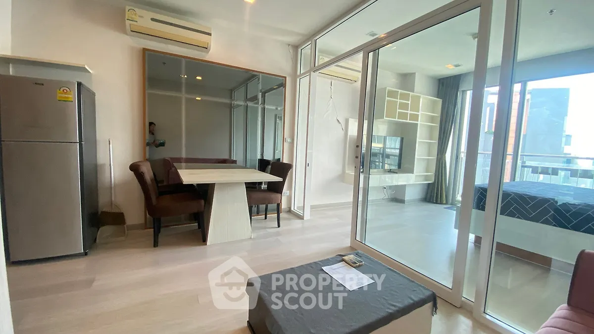 Modern open-plan living space with dining area and bedroom, featuring sleek furniture and large windows.