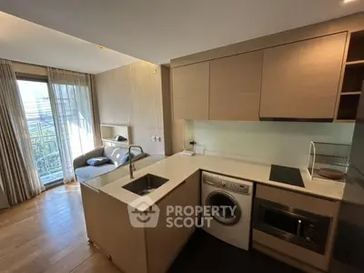 Modern kitchen with open layout and living area, featuring washing machine and sleek appliances.