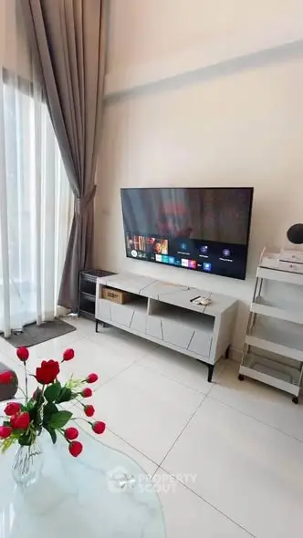 Modern living room with sleek TV setup and elegant decor, featuring a glass table with red roses.
