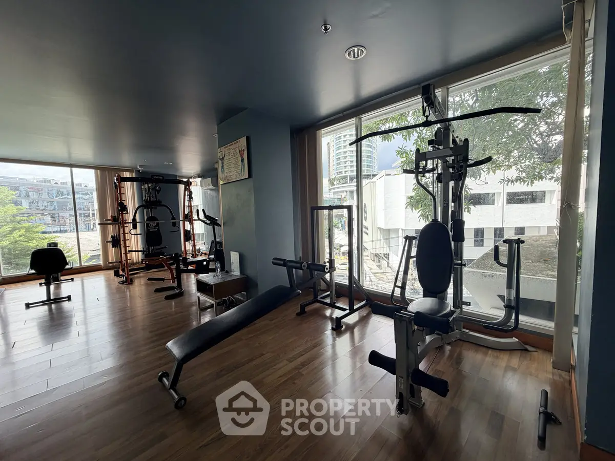 Spacious gym with modern equipment and large windows offering city views.