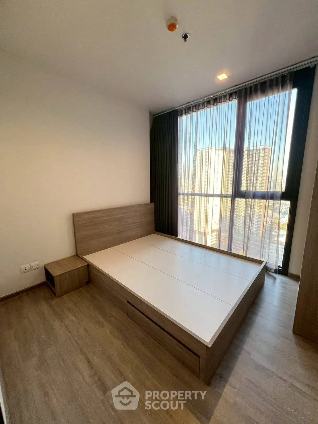 Spacious bedroom with large windows offering city views in modern apartment.