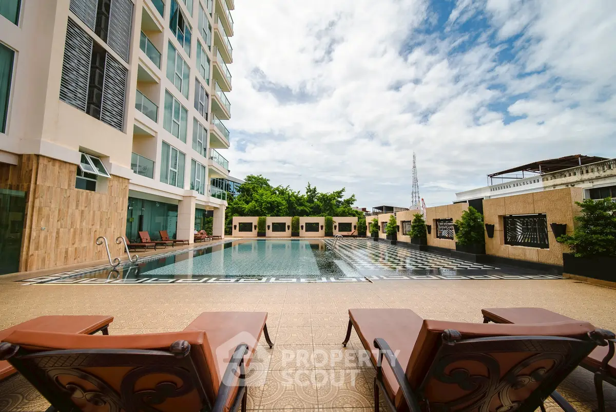 Luxurious apartment complex with a stunning outdoor pool and elegant lounge chairs under a clear sky.