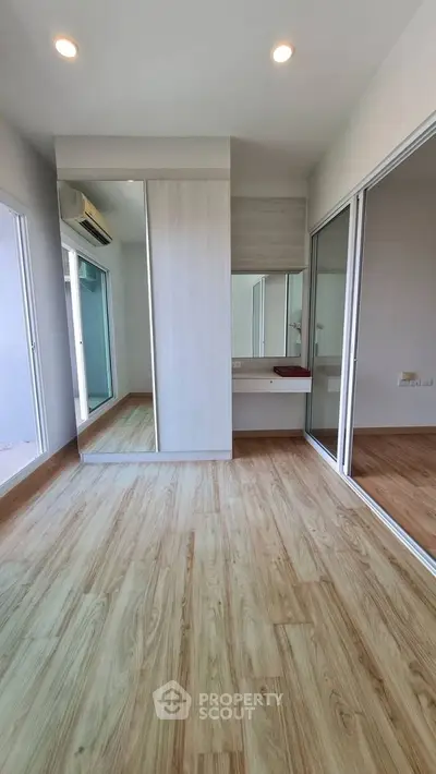 Spacious bedroom with wooden flooring and mirrored wardrobe in modern apartment.