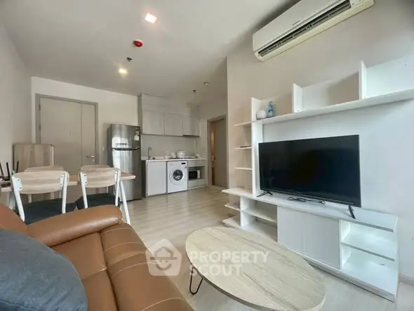 Modern living room with open kitchen, featuring sleek furniture and appliances.