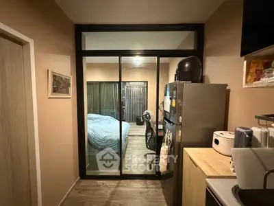 Modern apartment interior with bedroom view through glass partition, featuring sleek kitchen appliances.