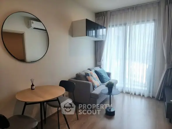 Modern living room with cozy sofa, round mirror, and natural light from large window.