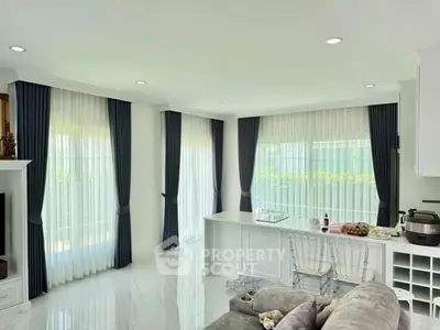 Elegant living room with large windows and modern decor, featuring a cozy seating area and stylish curtains.