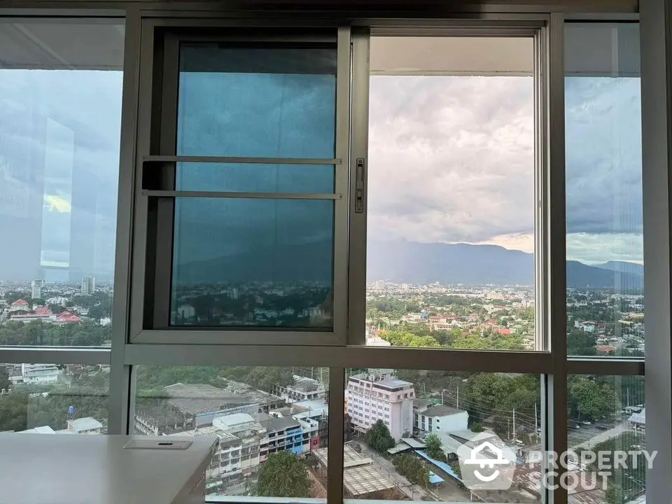 Stunning cityscape view from high-rise apartment window with mountains in the background.