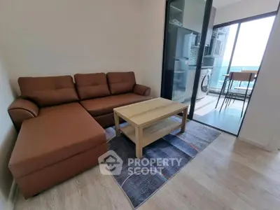 Modern living room with brown sectional sofa and wooden coffee table, leading to a balcony with a view.