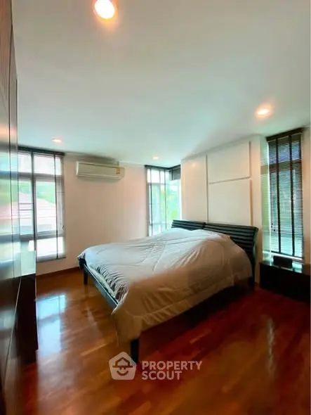 Spacious bedroom with wooden flooring and large windows offering natural light.