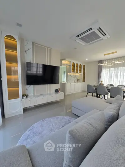 Modern living room with sleek design and dining area, featuring a large TV and elegant furnishings.