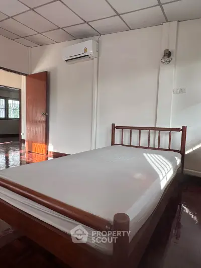 Spacious bedroom with wooden bed frame and air conditioning, perfect for comfortable living.