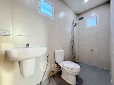 Modern bathroom with sleek fixtures and neutral tiles, featuring a shower and toilet.