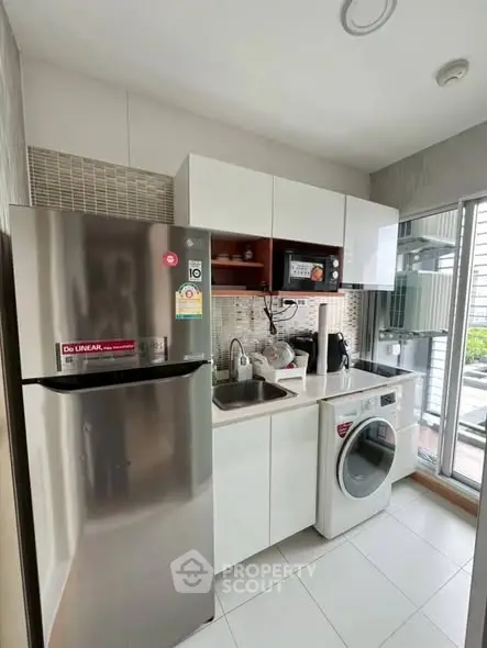 Modern compact kitchen with stainless steel fridge and washing machine in a bright apartment.