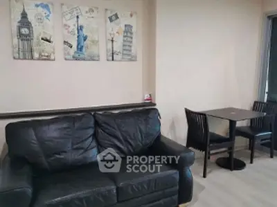 Cozy living room with black leather sofa and dining table, featuring travel-themed wall art.