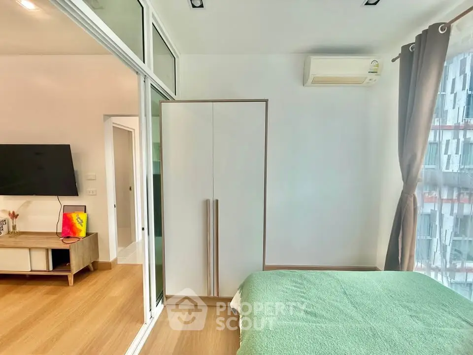 Modern bedroom with green bedding, large window, and air conditioning in a stylish apartment.