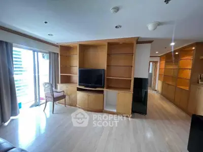 Spacious living room with built-in wooden shelves and large windows offering natural light.