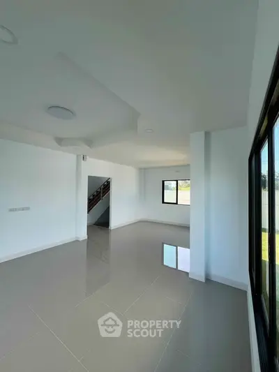 Spacious modern living room with large windows and glossy tiled floors in a bright home.
