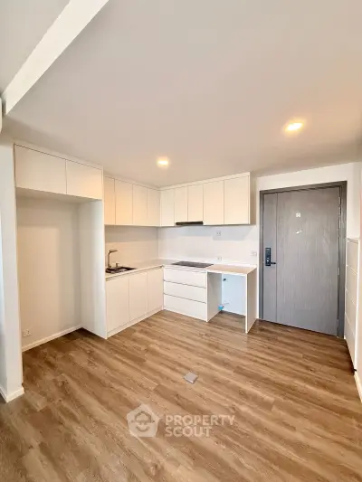 Modern minimalist kitchen with white cabinetry and wood flooring in a compact apartment.