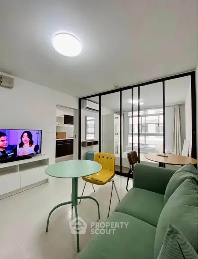 Modern living room with green sofa, TV, and dining area in open layout apartment.