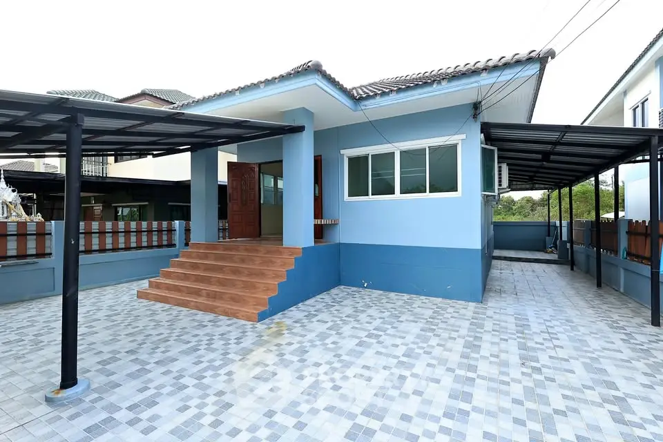 Charming blue single-story house with tiled patio and covered parking area.