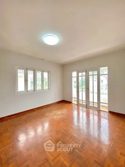 Spacious empty room with parquet flooring and large windows for natural light.