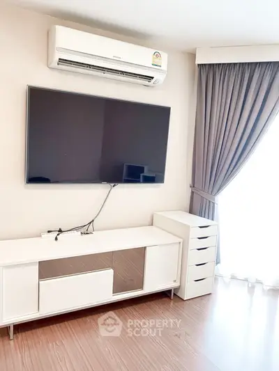 Modern living room with wall-mounted TV and air conditioning unit, featuring sleek white furniture and elegant curtains.