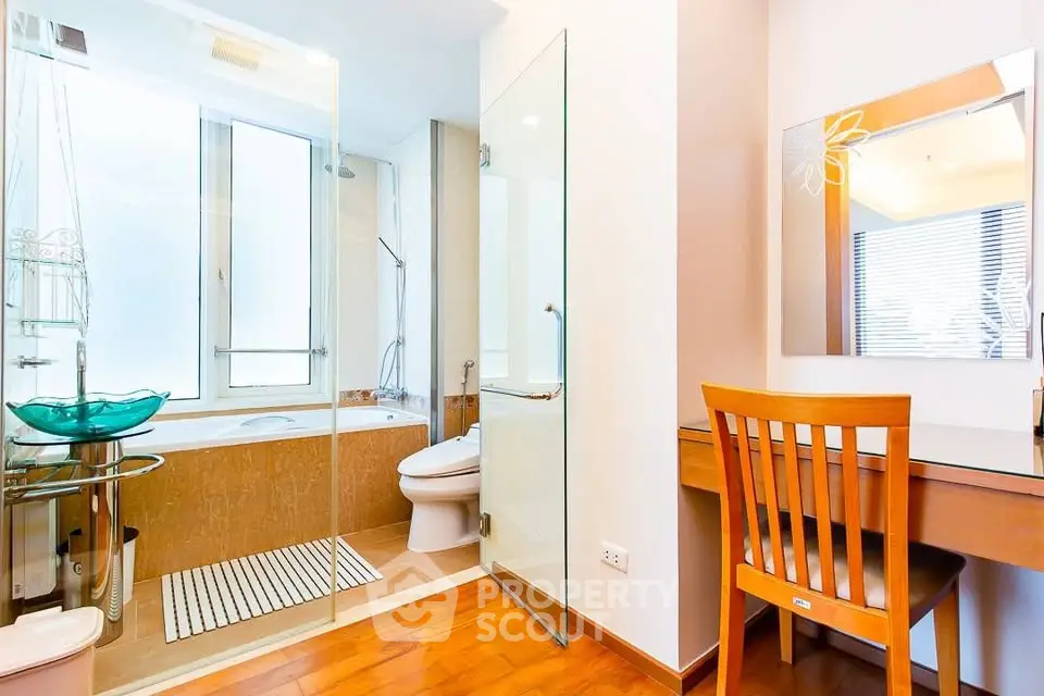 Modern bathroom with glass shower, bathtub, and wooden vanity desk.