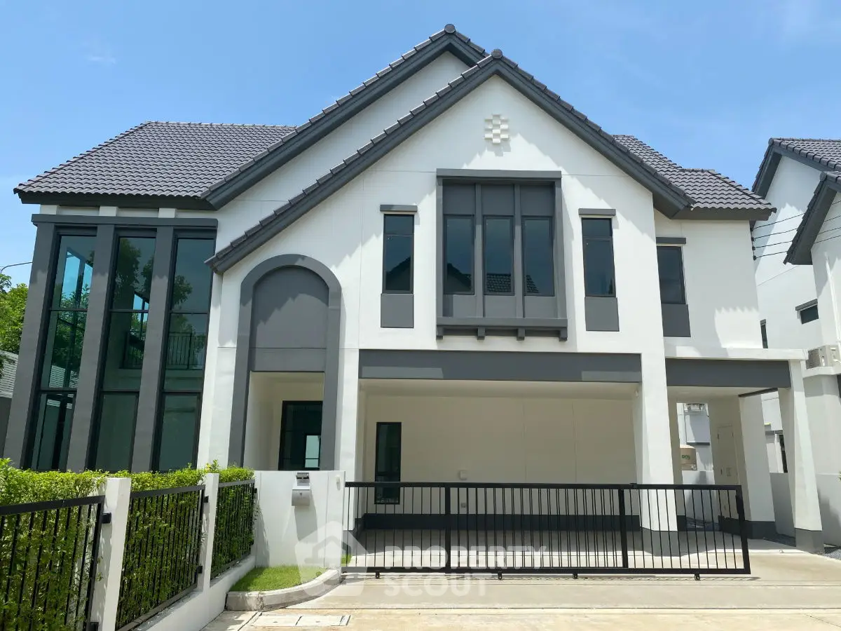 Modern two-story house with large windows and gated driveway in sunny neighborhood.