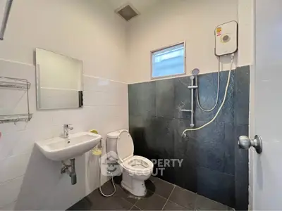 Modern bathroom with sleek black tiles and white fixtures, featuring a shower and compact sink.