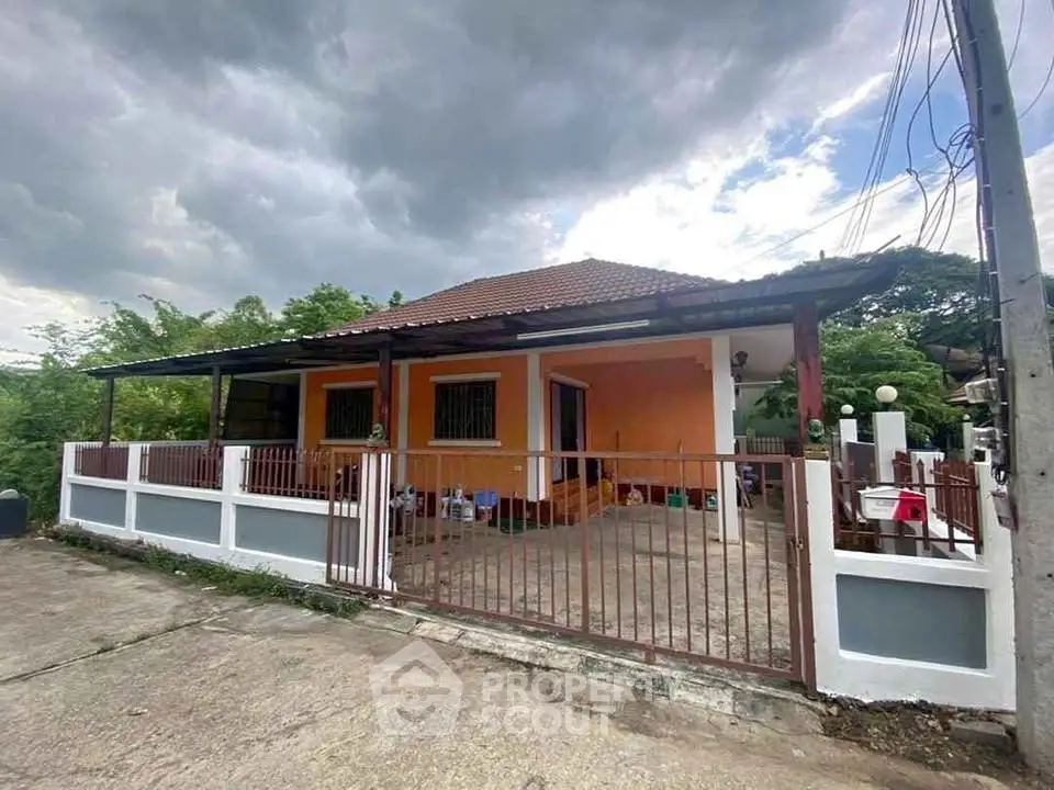 Charming single-story house with spacious front yard and gated entrance under cloudy skies.
