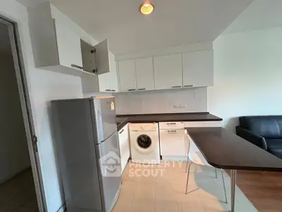 Modern kitchen with sleek cabinets, fridge, and washing machine in a compact open layout.