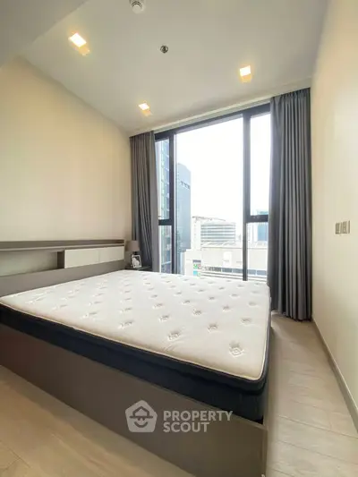 Modern bedroom with large window and city view, featuring a comfortable mattress and sleek design.
