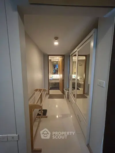 Modern hallway leading to a bathroom with sleek design and mirrored closet doors.