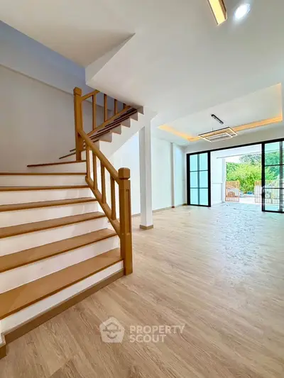 Spacious modern living room with wooden staircase and large windows opening to a garden view.