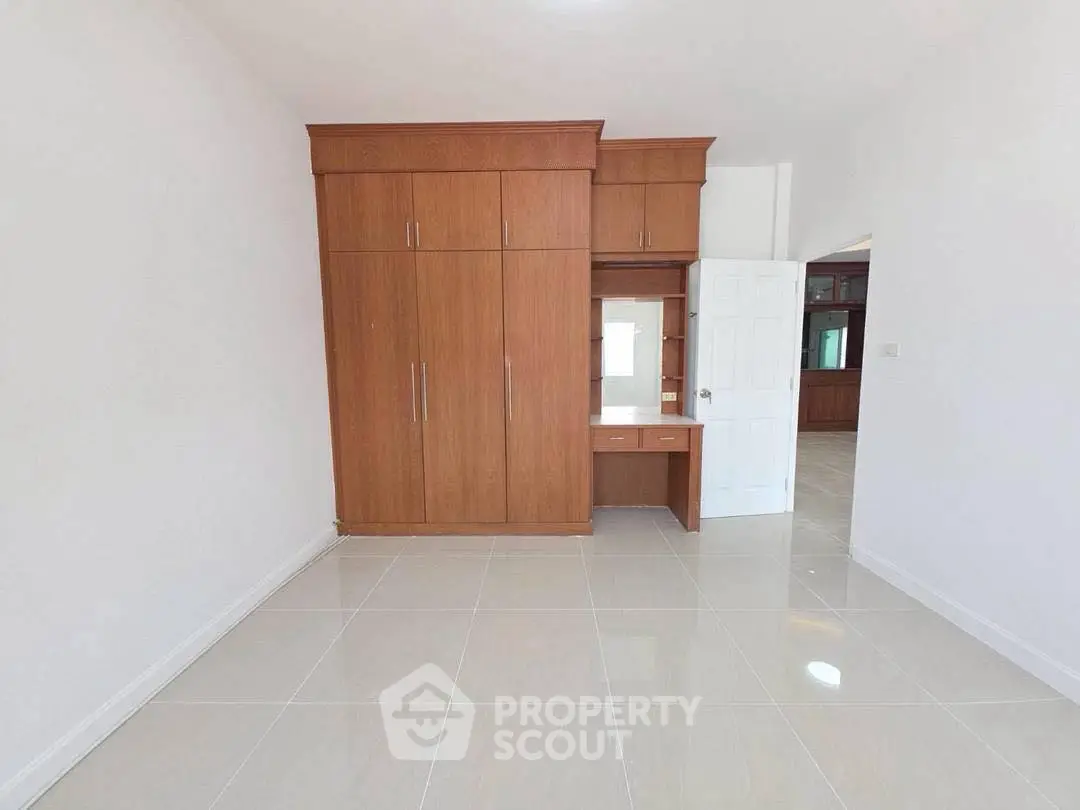 Spacious bedroom with built-in wooden wardrobe and glossy tiled floor, perfect for modern living.