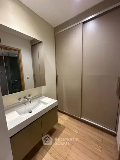 Modern bathroom with sleek vanity and sliding closet doors, featuring elegant wood flooring.