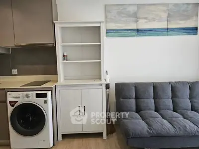 Modern living room with compact kitchen and stylish furniture, featuring a washing machine and cozy sofa.