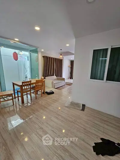 Spacious living room with modern dining area and cozy seating, featuring elegant lighting and large windows.
