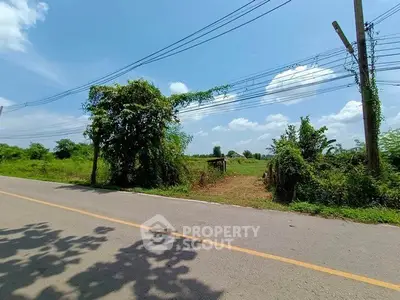 Scenic land plot with road access and lush greenery under a clear blue sky.