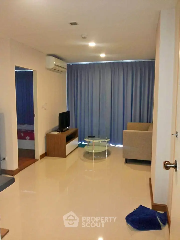 Modern living room with sleek furniture and large window draped with blue curtains.