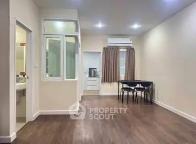 Spacious modern living area with wooden flooring and dining setup, adjacent to kitchen and bathroom.
