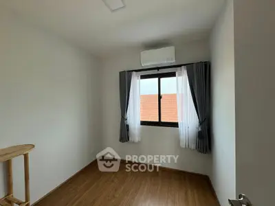 Bright bedroom with wooden flooring and large window, featuring modern air conditioning unit and elegant curtains.