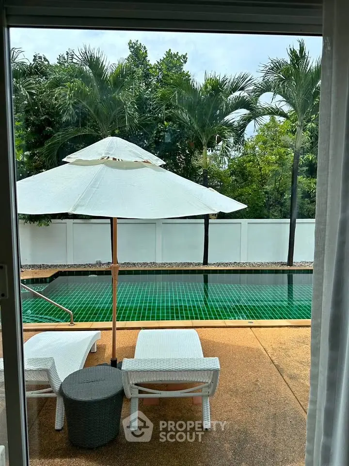 Luxurious poolside view with loungers and umbrella, surrounded by lush greenery, perfect for relaxation.