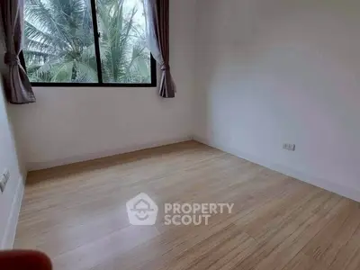 Spacious empty room with wooden flooring and large window with lush greenery view.