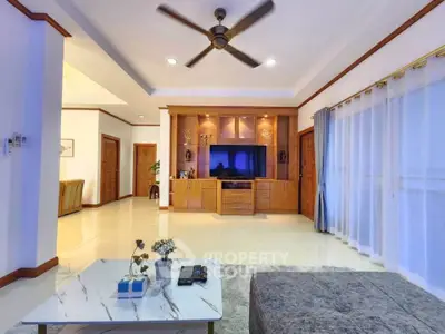 Spacious living room with modern decor and ceiling fan, featuring elegant wooden cabinetry and large windows.