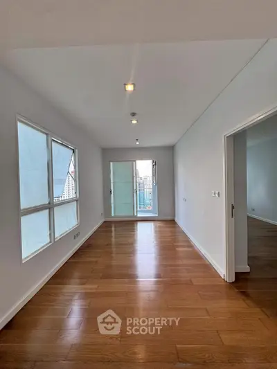 Spacious apartment interior with wooden flooring and large windows offering natural light.