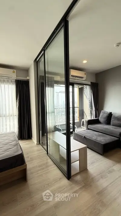Modern apartment with sliding glass doors separating bedroom and living area, featuring sleek furniture and natural light.