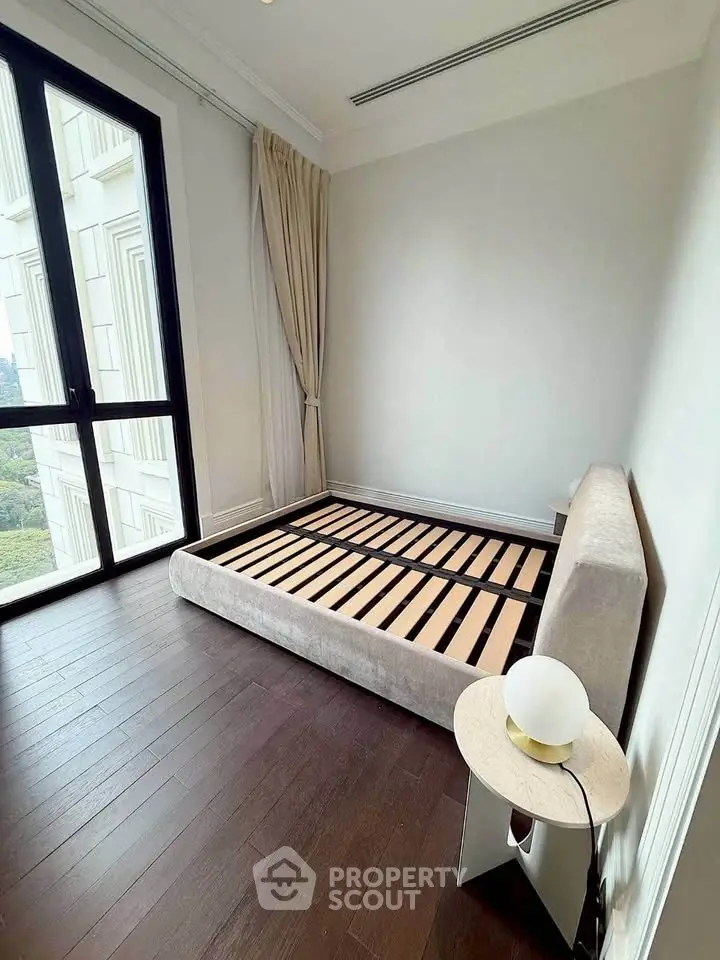 Spacious bedroom with large window and elegant bed frame in modern apartment.